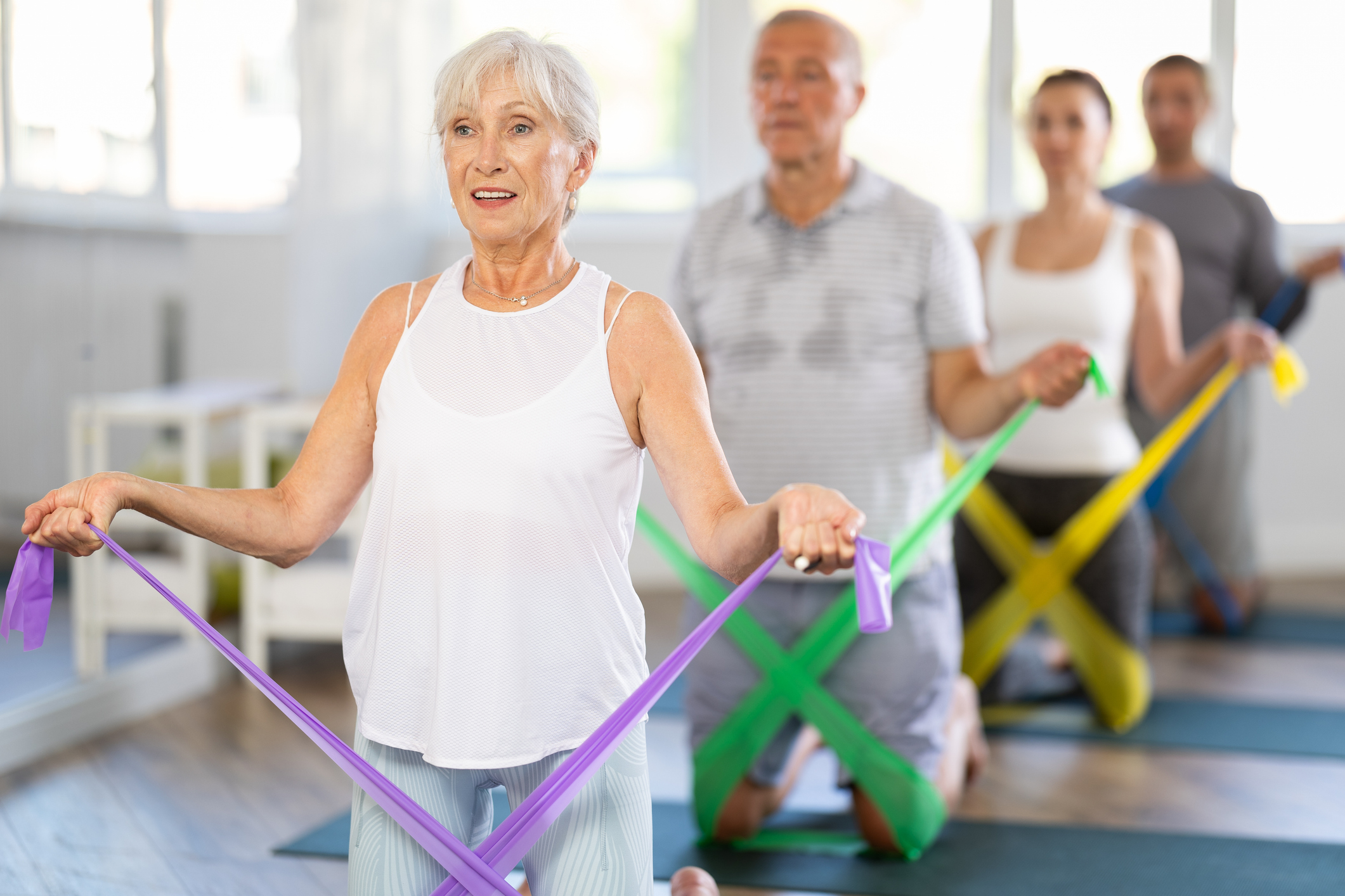 Elderly woman exercising with pilates elastic band on mat in group in studio