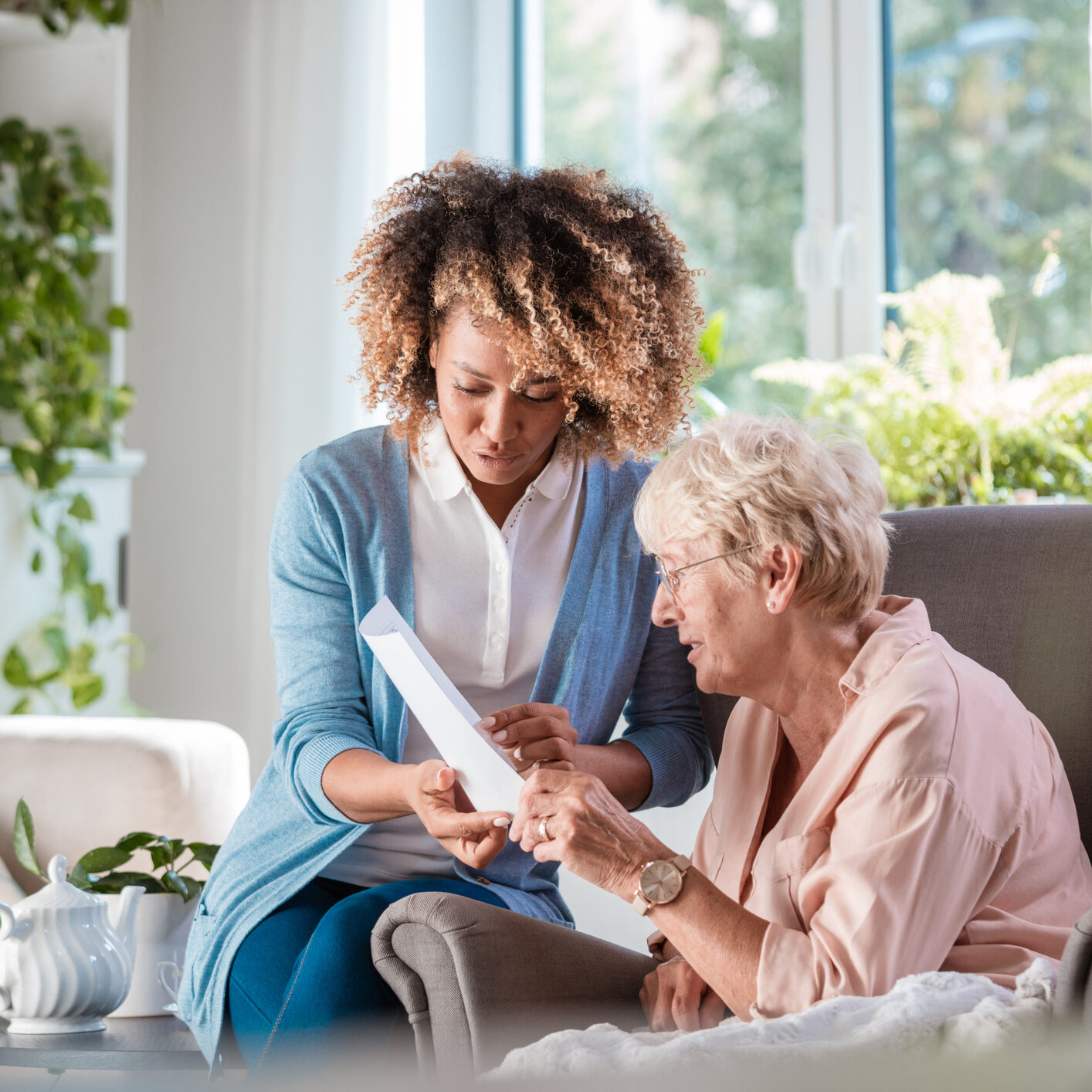 Female home caregiver supporting senior woman in her house, explaining her documents.